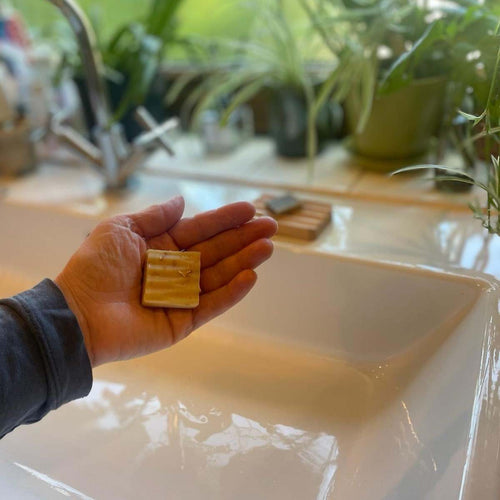 Small bar of College Green Lemongrass, Ginger and Beer soap held in a hand by  a bathroom sink. Size is suitable for Airbnbs, hotel rooms, guest bathrooms etc