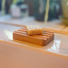 Small bar of College Green soap sat on a wooden soap dish on a white ceramic sink.