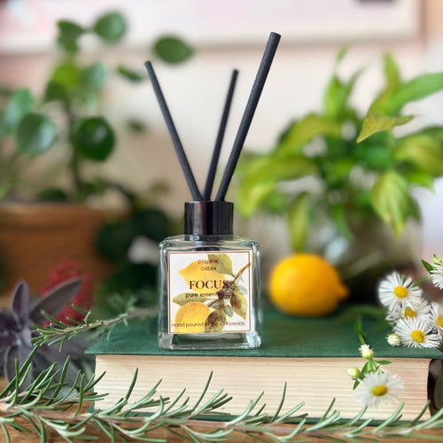 Focus essential oil reed diffuser with three black reeds, displayed with lemon, greenery and a book.