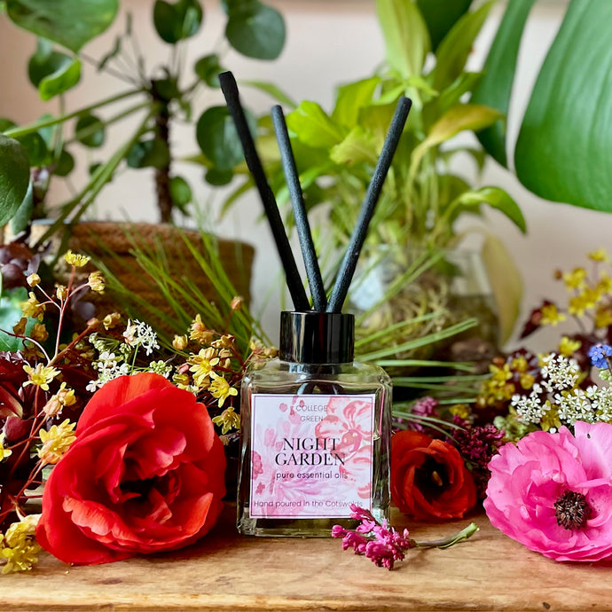 Diffuser with reeds surrounded by flowers and plants on a wooden surface

