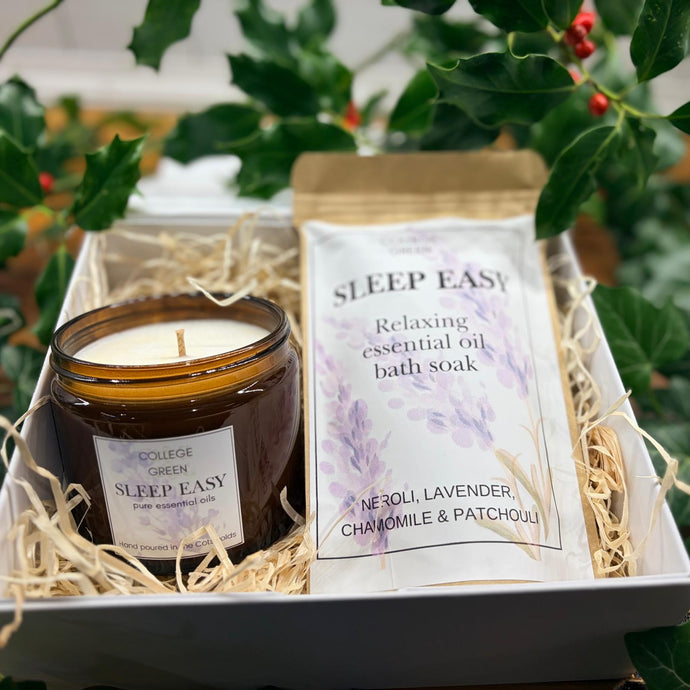 Sleep Easy candle and Sleep Easy bath soak nestled in a gift box surrounded by greenery
