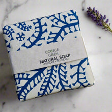 Wrapped bar of Lavender + Patchouli soap sat on a wooden soap dish