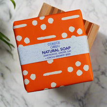 Wrapped bar of College Green Lemongrass, Ginger and Oat beer soap sat on a wooden soap dish